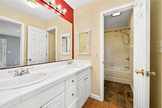 full bath with double vanity, a textured ceiling, baseboards, and a sink