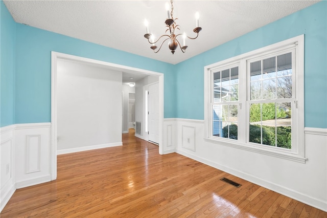 unfurnished dining area with light wood-type flooring, visible vents, and a chandelier