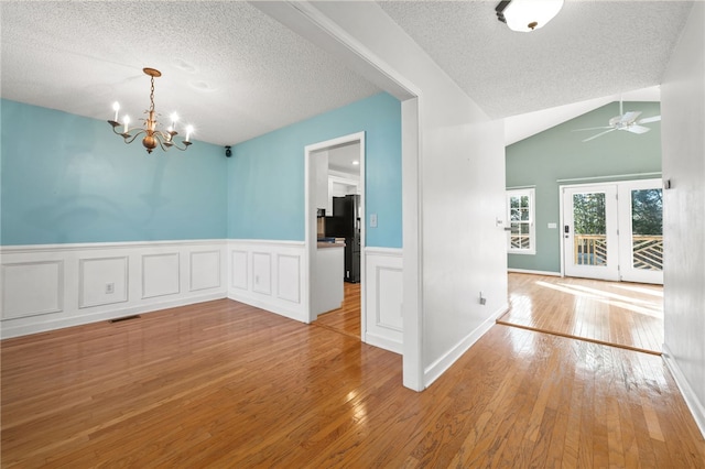 unfurnished dining area with visible vents, vaulted ceiling, a textured ceiling, light wood-type flooring, and ceiling fan with notable chandelier