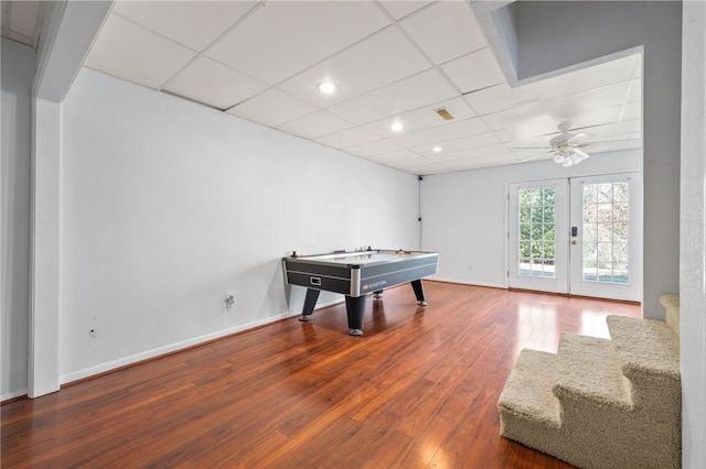 recreation room featuring french doors, a paneled ceiling, a ceiling fan, baseboards, and hardwood / wood-style flooring