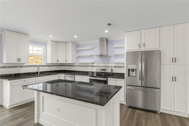 kitchen featuring white cabinetry, appliances with stainless steel finishes, a kitchen island, hardwood / wood-style flooring, and wall chimney range hood