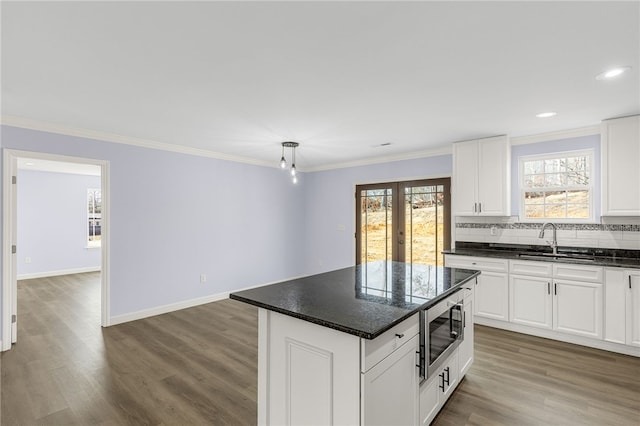 kitchen with stainless steel microwave, white cabinetry, sink, ornamental molding, and a center island