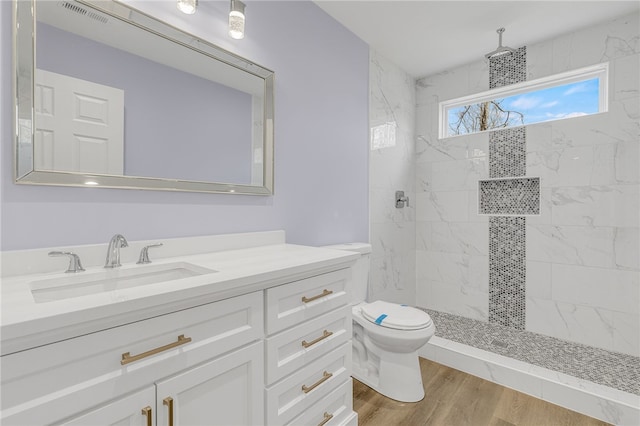 bathroom featuring hardwood / wood-style flooring, tiled shower, vanity, and toilet