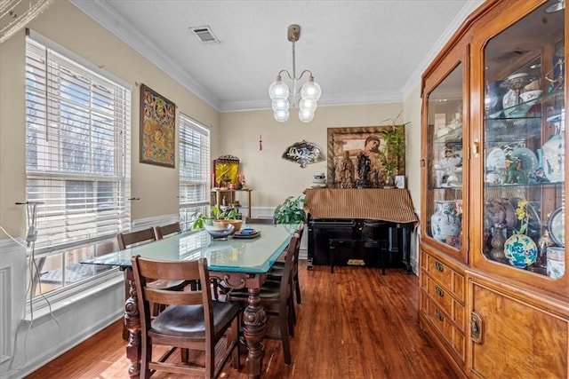 dining room with dark wood-type flooring, ornamental molding, and an inviting chandelier