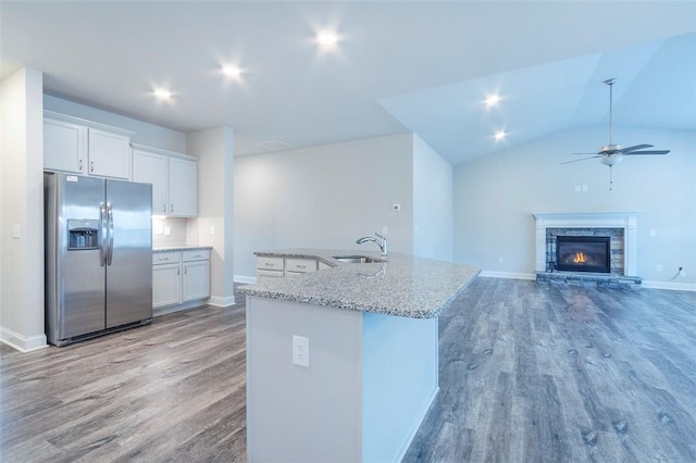 kitchen featuring stainless steel refrigerator with ice dispenser, sink, white cabinetry, a center island with sink, and light stone countertops