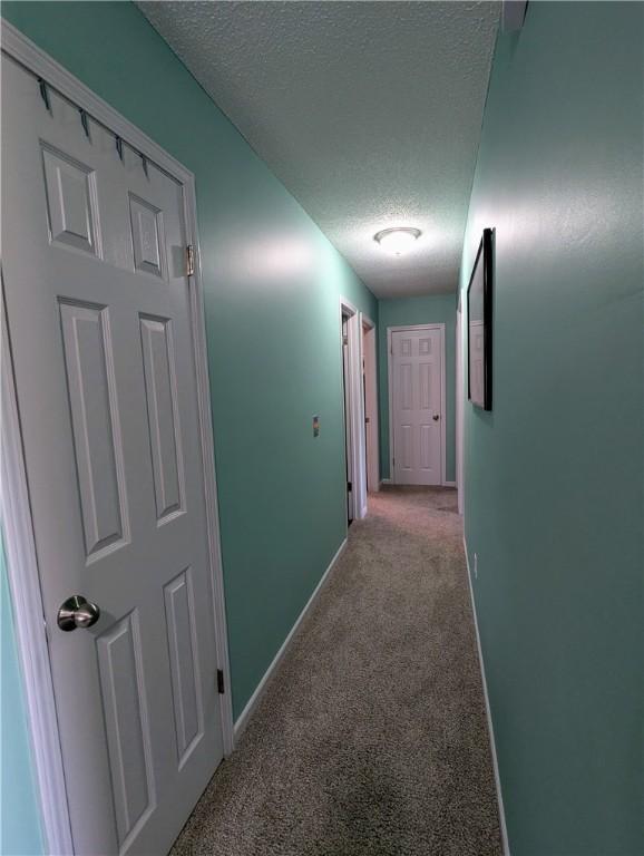 hallway featuring light colored carpet and a textured ceiling