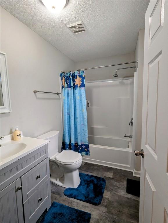 full bathroom featuring shower / bathtub combination with curtain, hardwood / wood-style flooring, vanity, a textured ceiling, and toilet