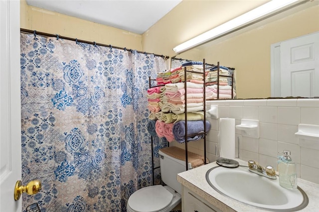 bathroom featuring walk in shower, vanity, toilet, and tile walls