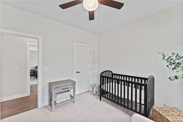 bedroom featuring a nursery area, carpet, and ceiling fan