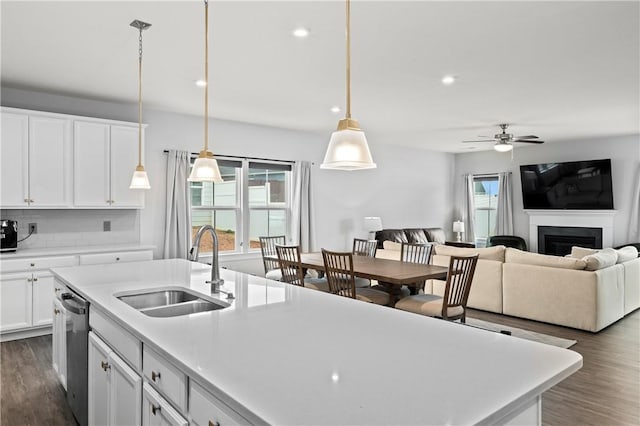 kitchen featuring decorative light fixtures, dishwasher, an island with sink, sink, and white cabinets