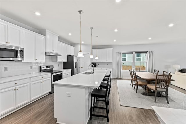 kitchen featuring sink, stainless steel appliances, an island with sink, white cabinets, and decorative light fixtures