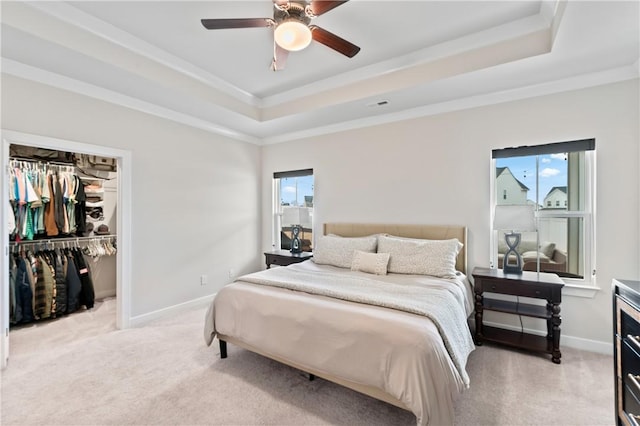 carpeted bedroom with crown molding, a walk in closet, ceiling fan, and a tray ceiling