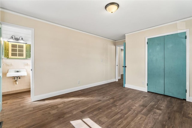 unfurnished bedroom with a sink, baseboards, dark wood finished floors, and crown molding