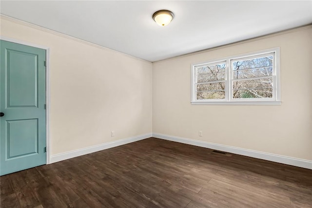 unfurnished room featuring dark wood-style floors, visible vents, ornamental molding, and baseboards