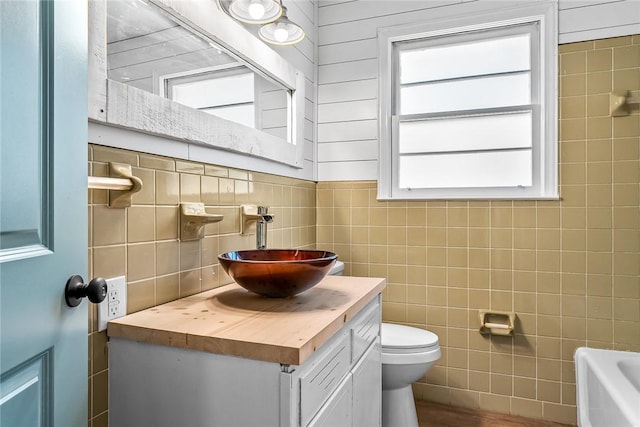 bathroom with toilet, tile walls, and vanity