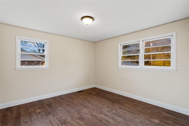 empty room with dark wood-style floors, visible vents, and baseboards