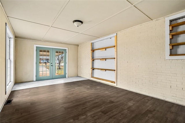 empty room with brick wall, french doors, dark wood-type flooring, and visible vents