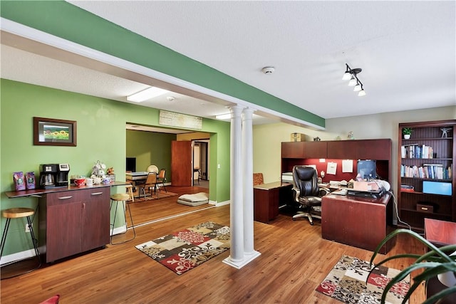 office space featuring a textured ceiling, decorative columns, light hardwood / wood-style floors, and beamed ceiling