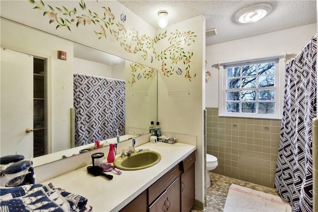 bathroom featuring tile walls, vanity, toilet, and a textured ceiling