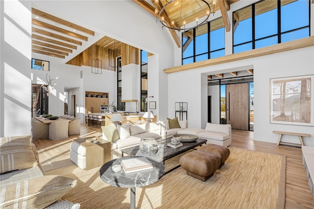 living room with beamed ceiling, a towering ceiling, an inviting chandelier, and light hardwood / wood-style flooring