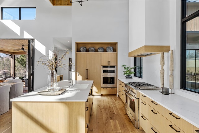 kitchen with premium range hood, sink, light brown cabinets, stainless steel appliances, and a center island with sink