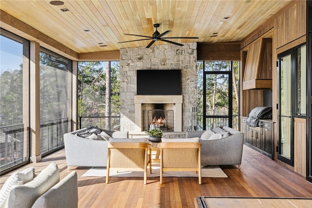 sunroom featuring ceiling fan, wooden ceiling, a wealth of natural light, and an outdoor stone fireplace