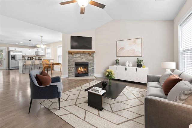 living room featuring wood-type flooring, lofted ceiling, a stone fireplace, and ceiling fan