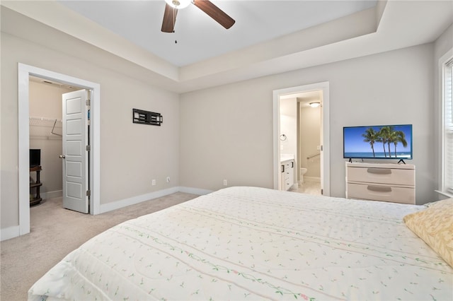 carpeted bedroom with a raised ceiling, ceiling fan, a spacious closet, and ensuite bath