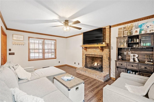 living room featuring a brick fireplace, hardwood / wood-style flooring, ornamental molding, and ceiling fan