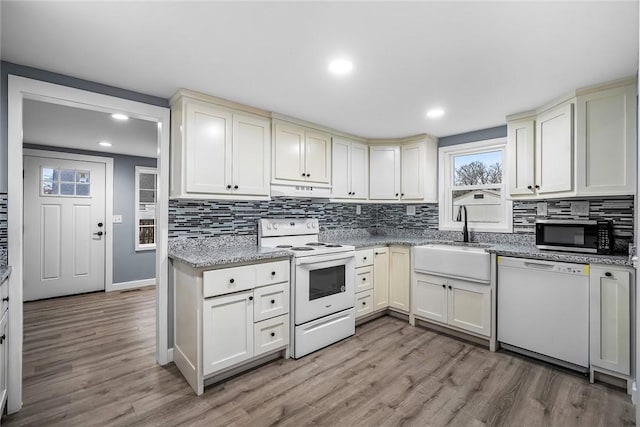 kitchen featuring sink, white appliances, light hardwood / wood-style flooring, and backsplash