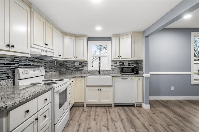 kitchen with sink, dark stone counters, decorative backsplash, white appliances, and light hardwood / wood-style flooring