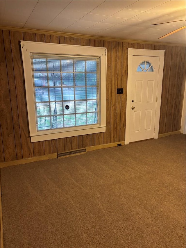 carpeted foyer entrance with crown molding and wood walls