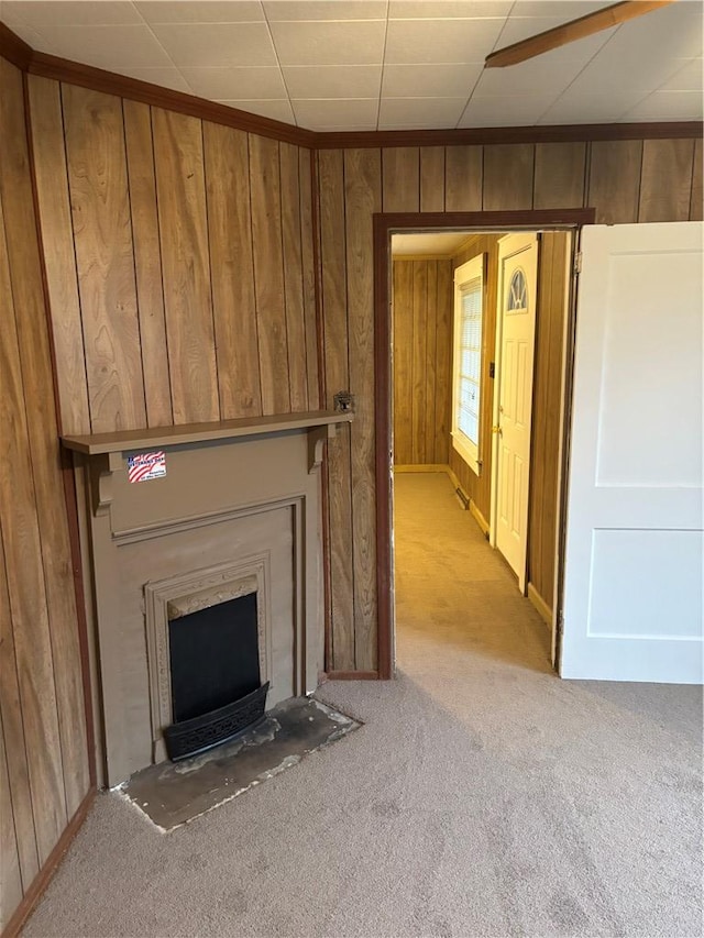 unfurnished living room featuring a fireplace, light colored carpet, and wood walls