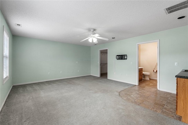 unfurnished bedroom featuring ceiling fan, ensuite bathroom, carpet flooring, a textured ceiling, and a spacious closet