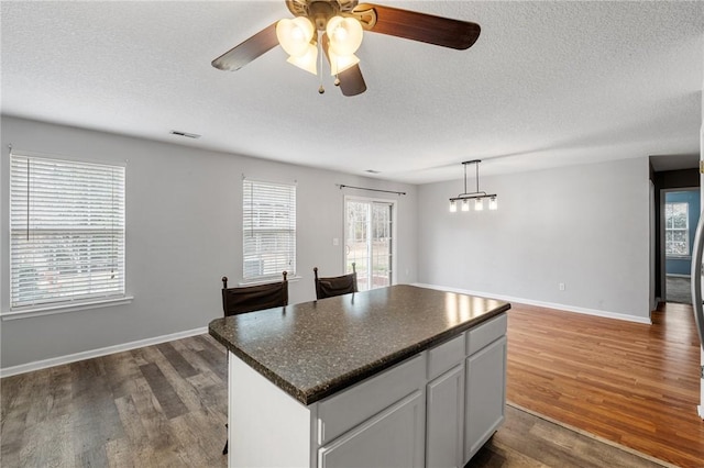 kitchen with dark hardwood / wood-style floors, pendant lighting, white cabinets, a center island, and a textured ceiling