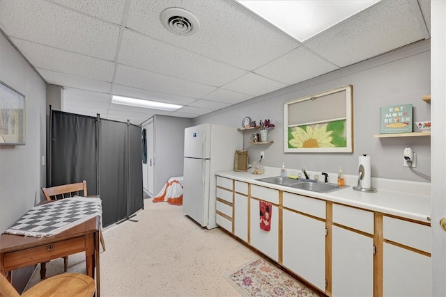 kitchen with white cabinetry, white fridge, sink, and a drop ceiling