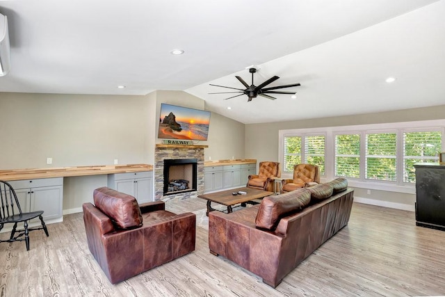 living room with a stone fireplace, built in desk, vaulted ceiling, light hardwood / wood-style flooring, and ceiling fan