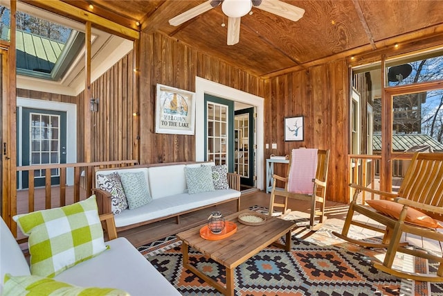 living room featuring a skylight, ceiling fan, and wood walls