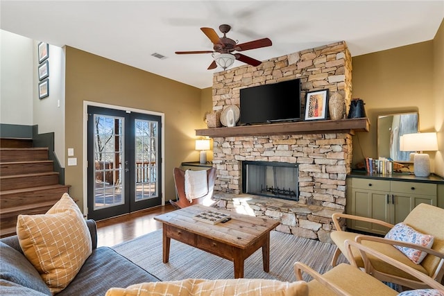 living room featuring french doors, a stone fireplace, ceiling fan, and light hardwood / wood-style flooring