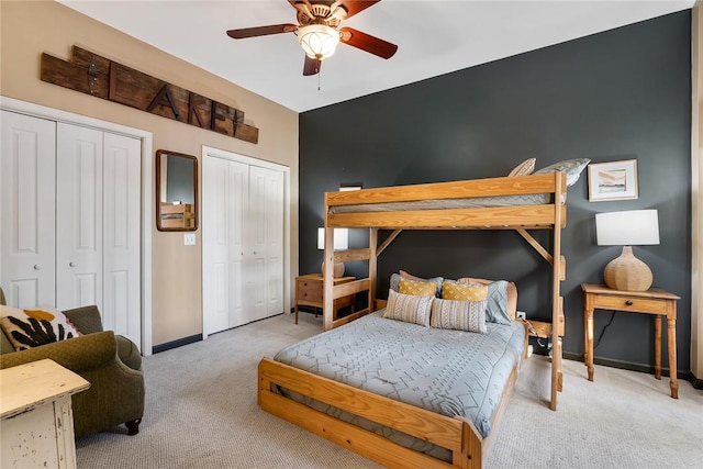 bedroom with light carpet, ceiling fan, and multiple closets