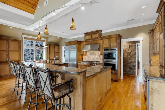 kitchen with appliances with stainless steel finishes, a kitchen bar, dark stone counters, hanging light fixtures, and a large island