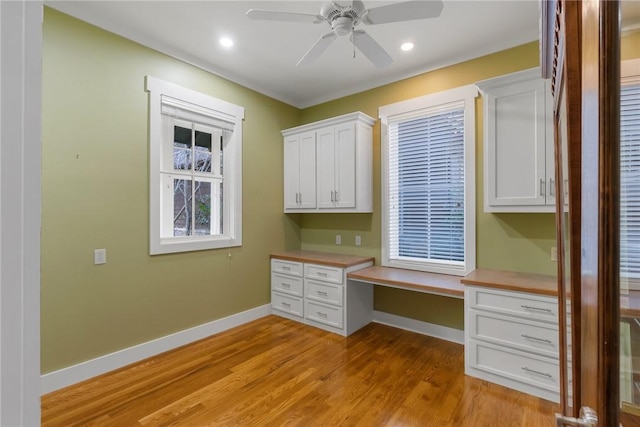 unfurnished office featuring ceiling fan, built in desk, and light hardwood / wood-style floors