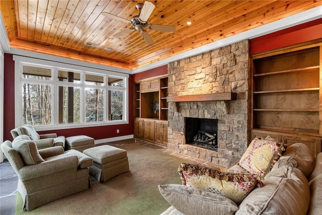 carpeted living room featuring built in shelves, a stone fireplace, wood ceiling, a tray ceiling, and ceiling fan