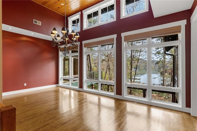 entryway featuring a water view, wooden ceiling, a notable chandelier, hardwood / wood-style flooring, and a high ceiling