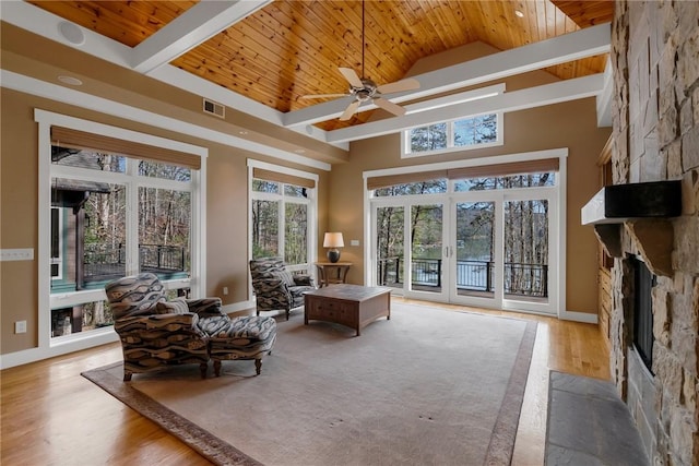 living area with a stone fireplace, high vaulted ceiling, wooden ceiling, light wood-type flooring, and french doors
