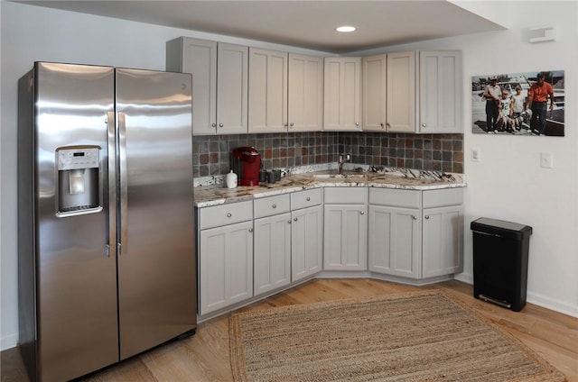 kitchen featuring light stone countertops, a sink, light wood-style floors, stainless steel refrigerator with ice dispenser, and decorative backsplash