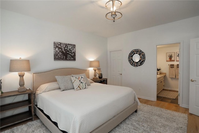 bedroom with light wood-type flooring, ensuite bath, and baseboards