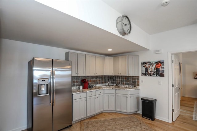 kitchen with light wood finished floors, stainless steel fridge, tasteful backsplash, light stone counters, and a sink