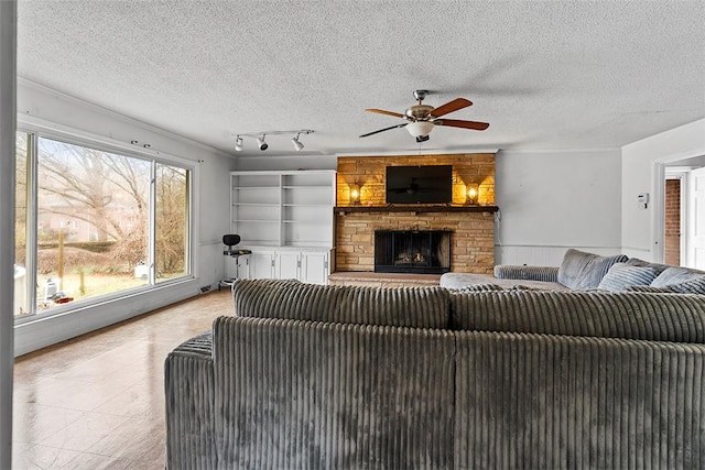 living room with ceiling fan, a stone fireplace, a textured ceiling, and rail lighting