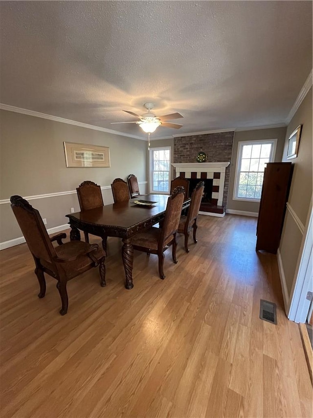 dining room with ornamental molding, a brick fireplace, a healthy amount of sunlight, and light wood-type flooring